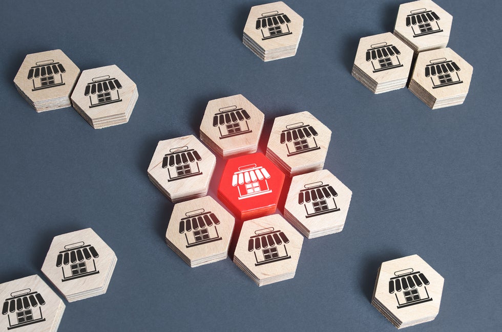 Numerous small hexagonal pieces, each colored gray and displaying a symbol of a store, are shown in physically dispersed groups, but all such pieces and groups appear to emanate from a red hexagonal piece in the center, which represents a franchisor-type role.