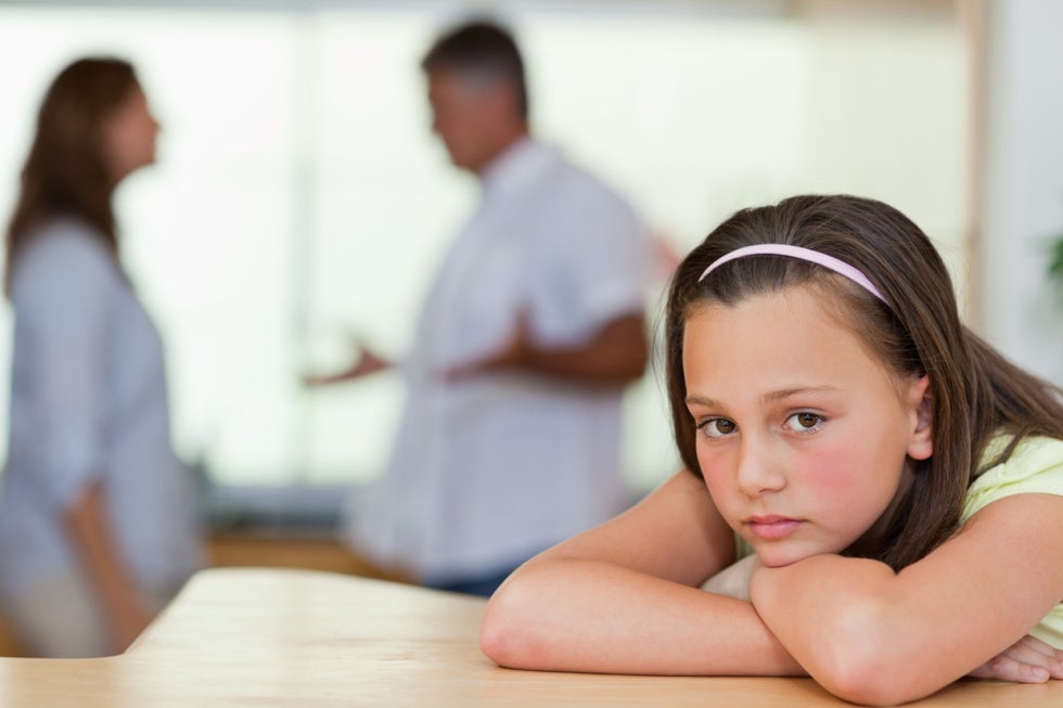 sad young girl with parents arguing in background