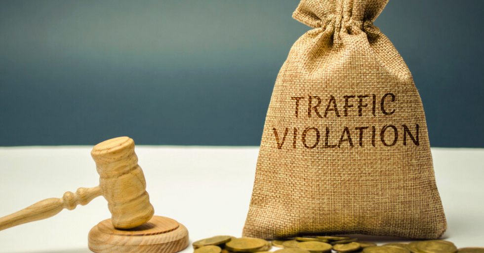 A photo of a bag of coins with the words "Traffic Violation" written on it, sitting next to a gavel.