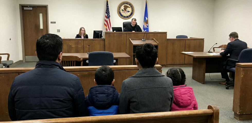 Family of four seated in an immigration courtroom facing a judge; illustrates how a USCIS denial can lead to removal proceedings.