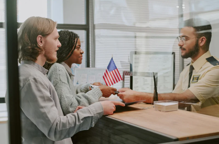 A couple hands their documents to a border control officer behind a counter