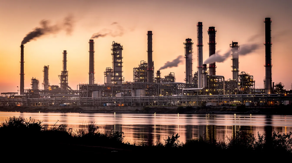 The image depicts an industrial refinery situated along a river at sunset, with prominent smoke stacks and extensive piping silhouetted against the colorful sky. This scene highlights the work environment that can pose risks for injured workers, potentially leading to workers compensation claims due to common workplace injuries.
