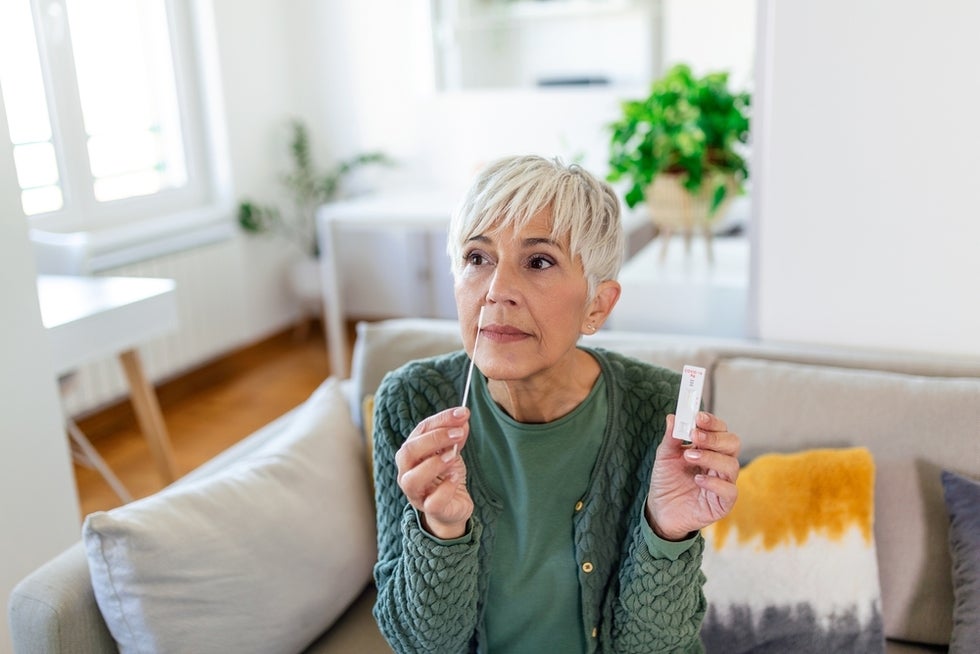 Woman sitting on sofa holding at-home COVID test.