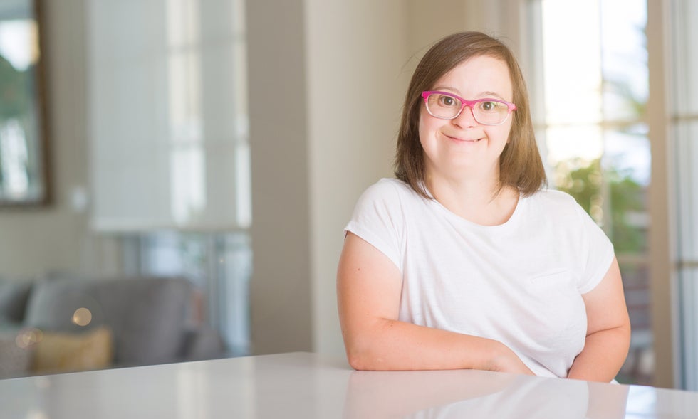 Woman with Down Syndrome wearing eyeglasses and sitting at kitchen counter in her home.