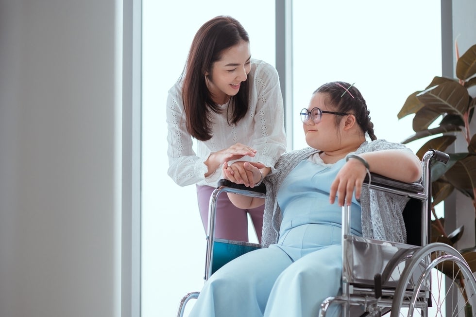 Girl with Down syndrome sitting in wheelchair and interacting with caregiver.