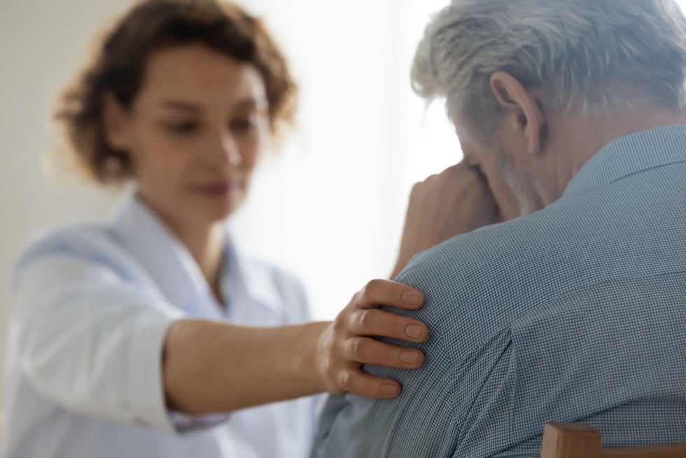 Female health professional comforting upset senior male patient.