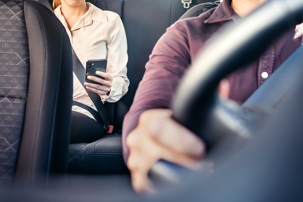 A rideshare passenger uses a cell phone to ask her lawyer how to file a California rideshare accident lawsuit while the driver steers the vehicle.