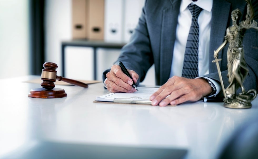 A lawyer in a suit sits at a desk and fills out paperwork, which is one thing that a truck accident lawyer does for a client.