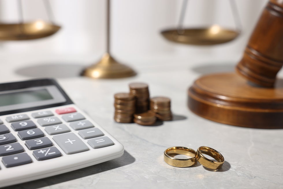 Two gold wedding rings next to a calculator, coins, and a legal scale, representing divorce asset division.