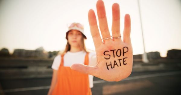 Protestor holds up hand to camera with message written on hand, stating "Stop Hate"
