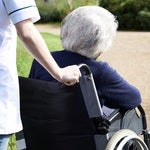nurse gently pushing an elder woman's wheelchair