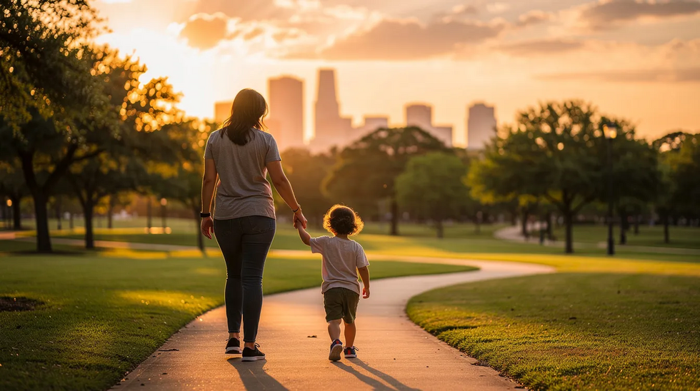 A parent is gently holding the hand of a young child while walking through a Houston park at sunset, symbolizing the nurturing aspects of the parent-child relationship. This scene reflects the importance of establishing legal parentage and the emotional connections that play a vital role in a child's life.