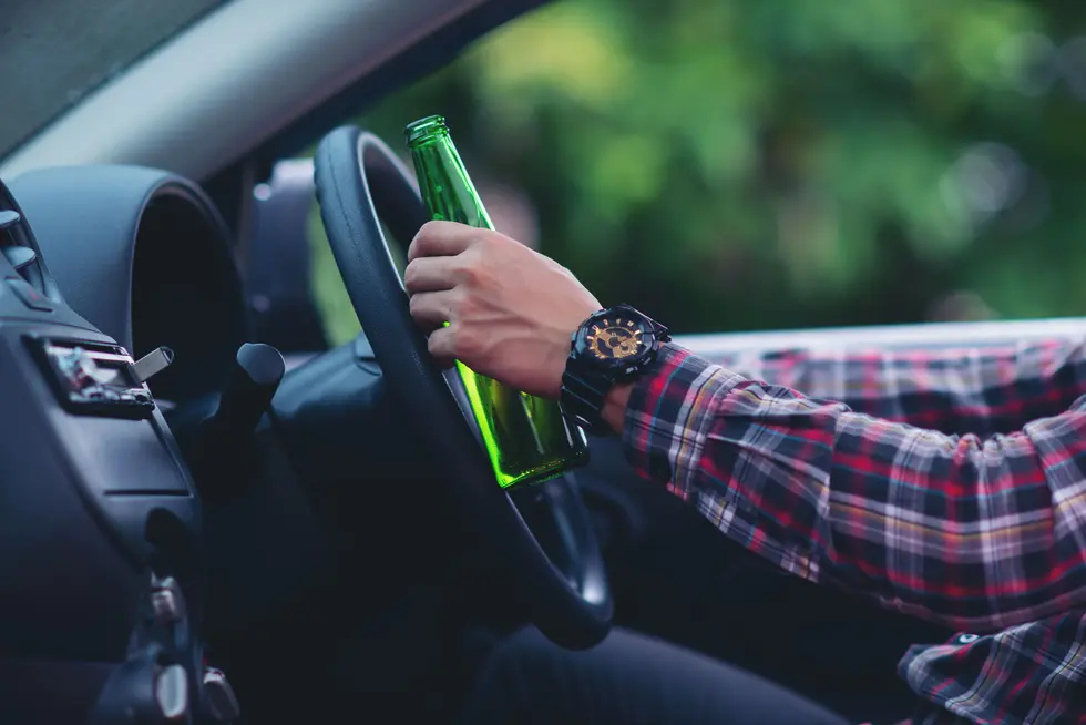 Close-up of a person holding a green bottle while driving a car, emphasizing the dangers of driving under influence. Learn about the difference between DUI and DWI in NJ.