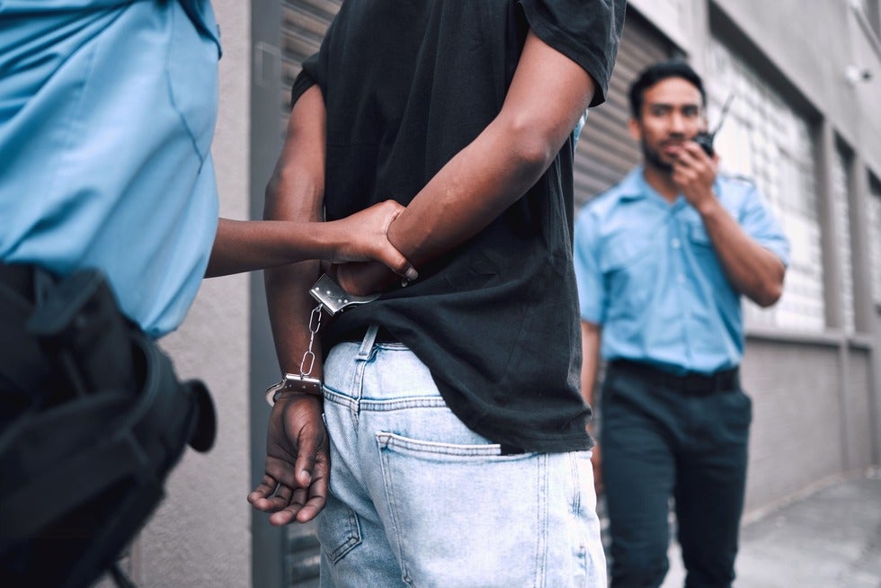 A man is restrained by two police officers in Manasquan, New Jersey, highlighting a law enforcement situation.