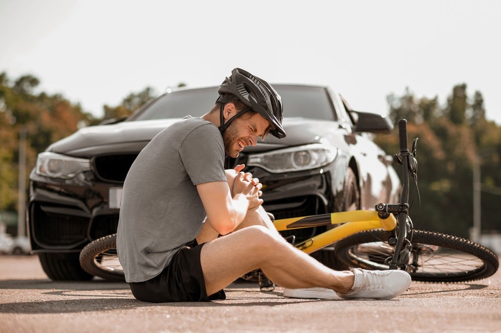 A man sits on the ground beside his bike after being hit by a car, highlighting a need personal injury law services in Manasquan, New Jersey.
