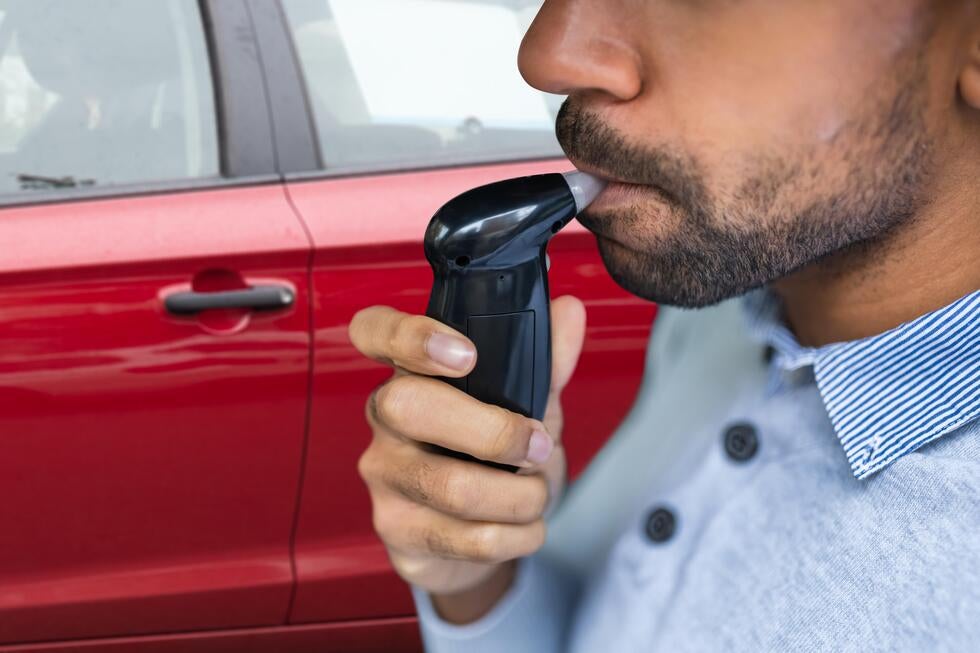 Man using breathalyzer device next to a car, representing DUI and criminal law defense in Ship Bottom, NJ