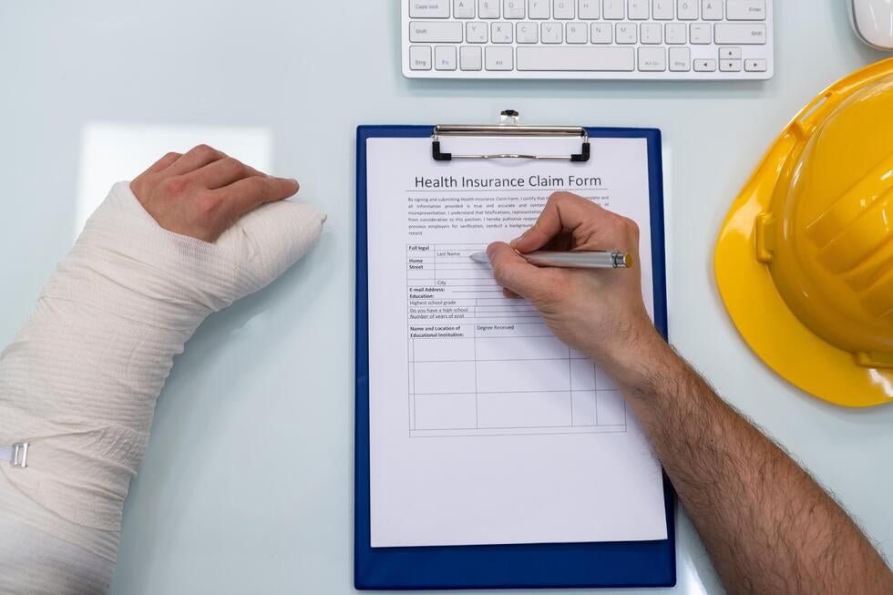 Injured construction worker with arm in bandage filling out a health insurance claim form, showing personal injury cases in Stafford, NJ