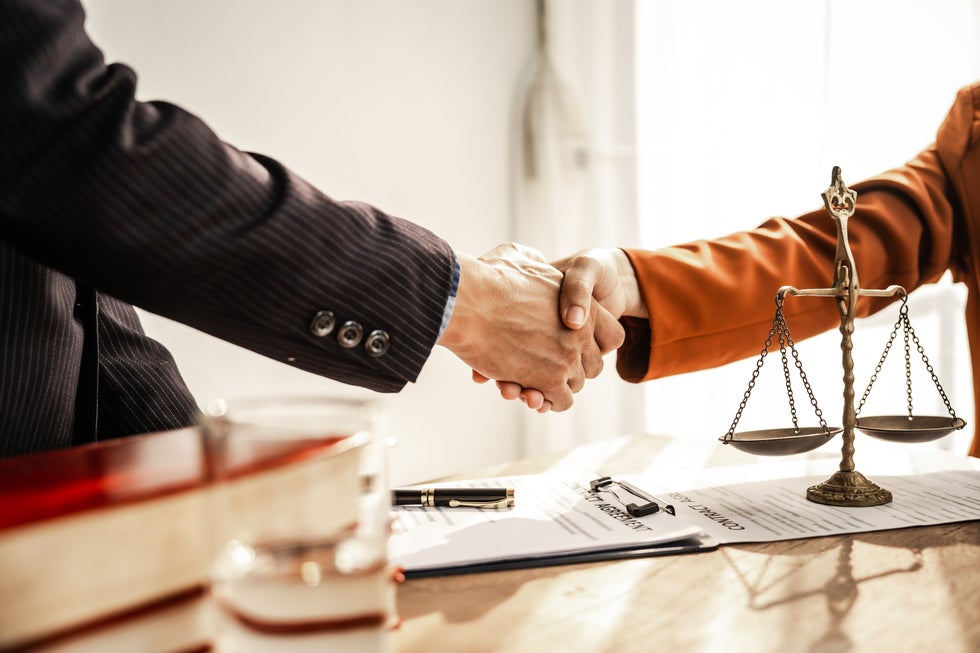  Lawyer and client shaking hands over legal documents with justice scale on desk, reflecting full legal services in Stafford, NJ