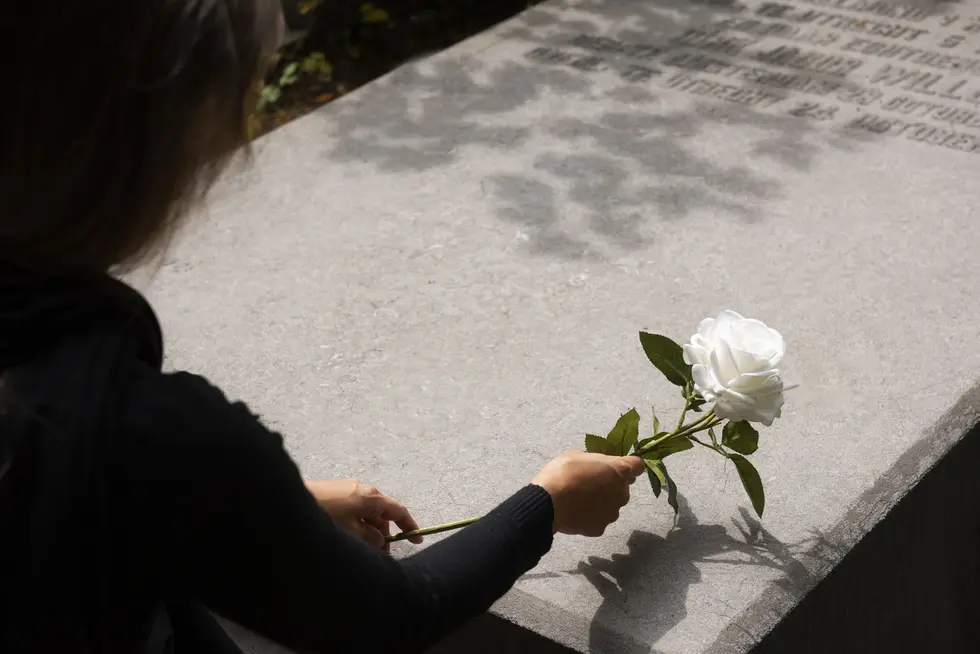 A woman gently places a white rose on a grave, honoring a loved one lost to wrongful death