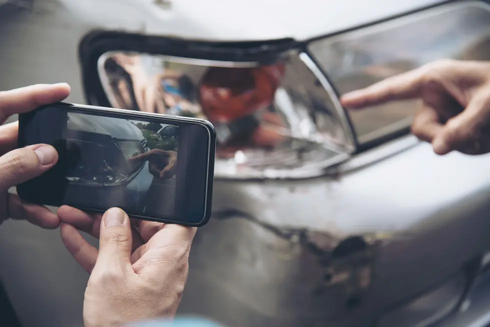 A person photographing a car with a broken headlight, highlighting potential evidence for a ride share accident case in New Jersey.