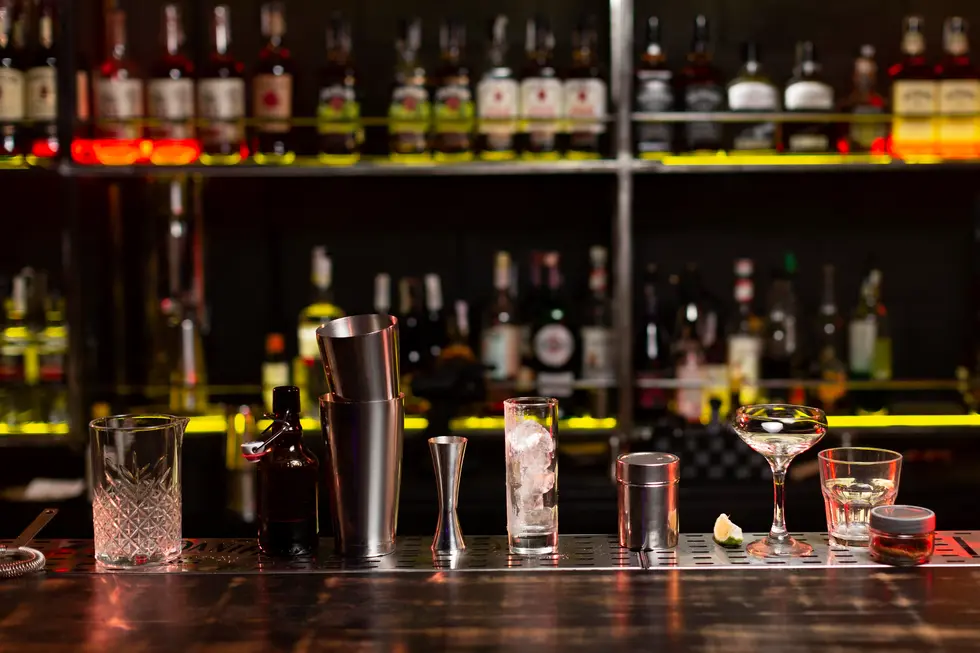 Bar counter with cocktail shakers and glassware in front of a fully stocked liquor shelf, representing the process of selling a retail liquor license in New Jersey