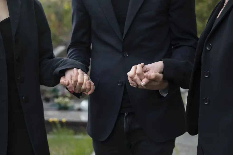Three people holding hands in a cemetery, symbolizing support and remembrance during a time of loss.