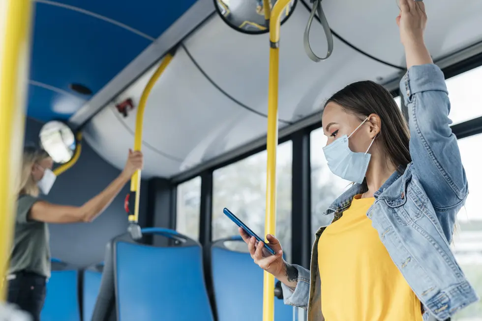 Masked passenger standing on a New Jersey public bus holding the overhead rail