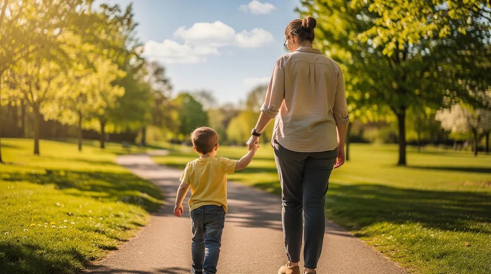 The image depicts a parent gently holding a child's hand while strolling through a sunny park, symbolizing the importance of the parent-child relationship in maintaining emotional connections. This scene highlights the significance of positive parenting time, especially in the context of custody orders and visitation rights as outlined in Texas family law.