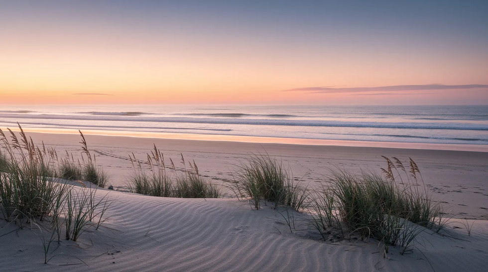 The image depicts a serene Cape Cod beach at sunrise, featuring gentle waves lapping at the shore and sea grass swaying softly in the morning breeze. This tranquil scene evokes a sense of peace, much like the calmness one might seek during divorce proceedings or family court matters in Massachusetts.