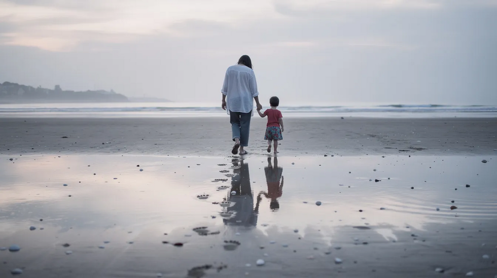 A parent and child walk hand-in-hand along a serene beach at low tide, with gentle waves lapping at the shore. The scene captures a moment of connection and tranquility, reflecting the joy of family time amidst nature.