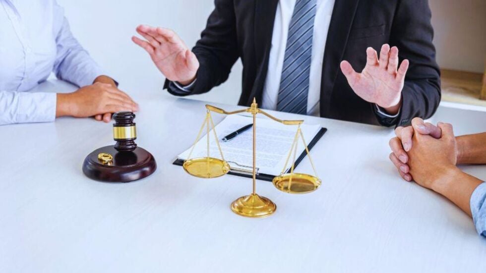 Divorce lawyer in a suit sits between a couple at a conference table, with a gavel, wedding rings, legal document, and golden scales of justice in front, discussing prenuptial agreement issues in a Miami athlete divorce.