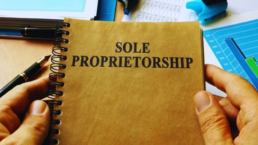 Person holding a notebook labeled “Sole Proprietorship,” surrounded by financial documents, charts, and office supplies, representing a sole proprietorship business structure.