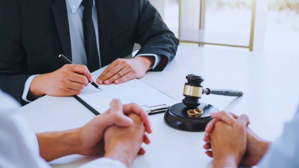 Divorce and business ownership lawyer in Miami meeting with a couple, signing documents at a desk with a judge’s gavel and wedding rings visible, representing legal guidance in divorce proceedings.