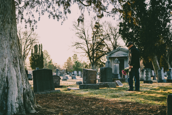 Person holding flowers while visiting a loved one’s grave in a cemetery, symbolizing loss and remembrance in a wrongful death case.