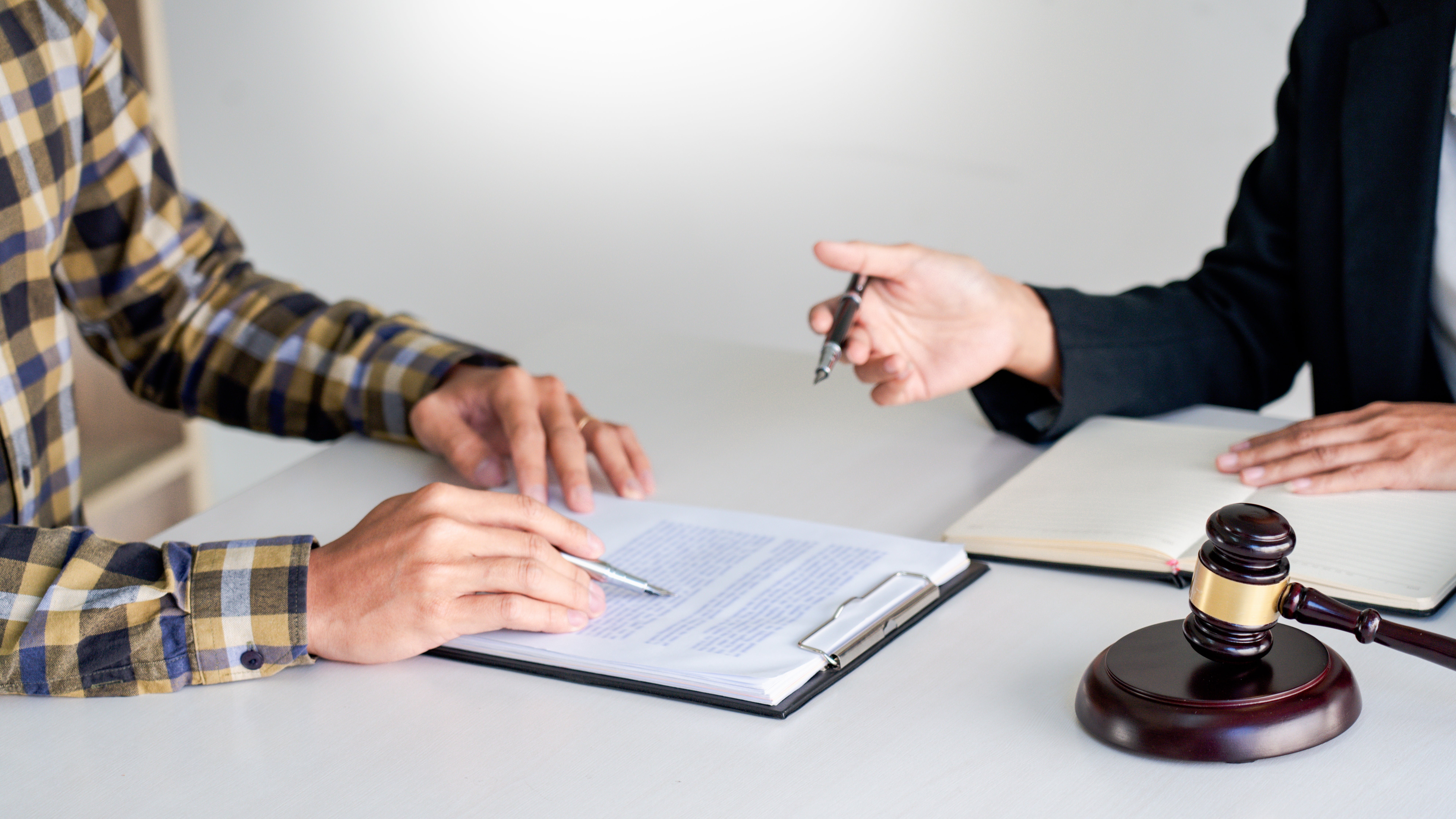 Close-up of attorney and client reviewing and signing legal documents with gavel on desk during consultation.