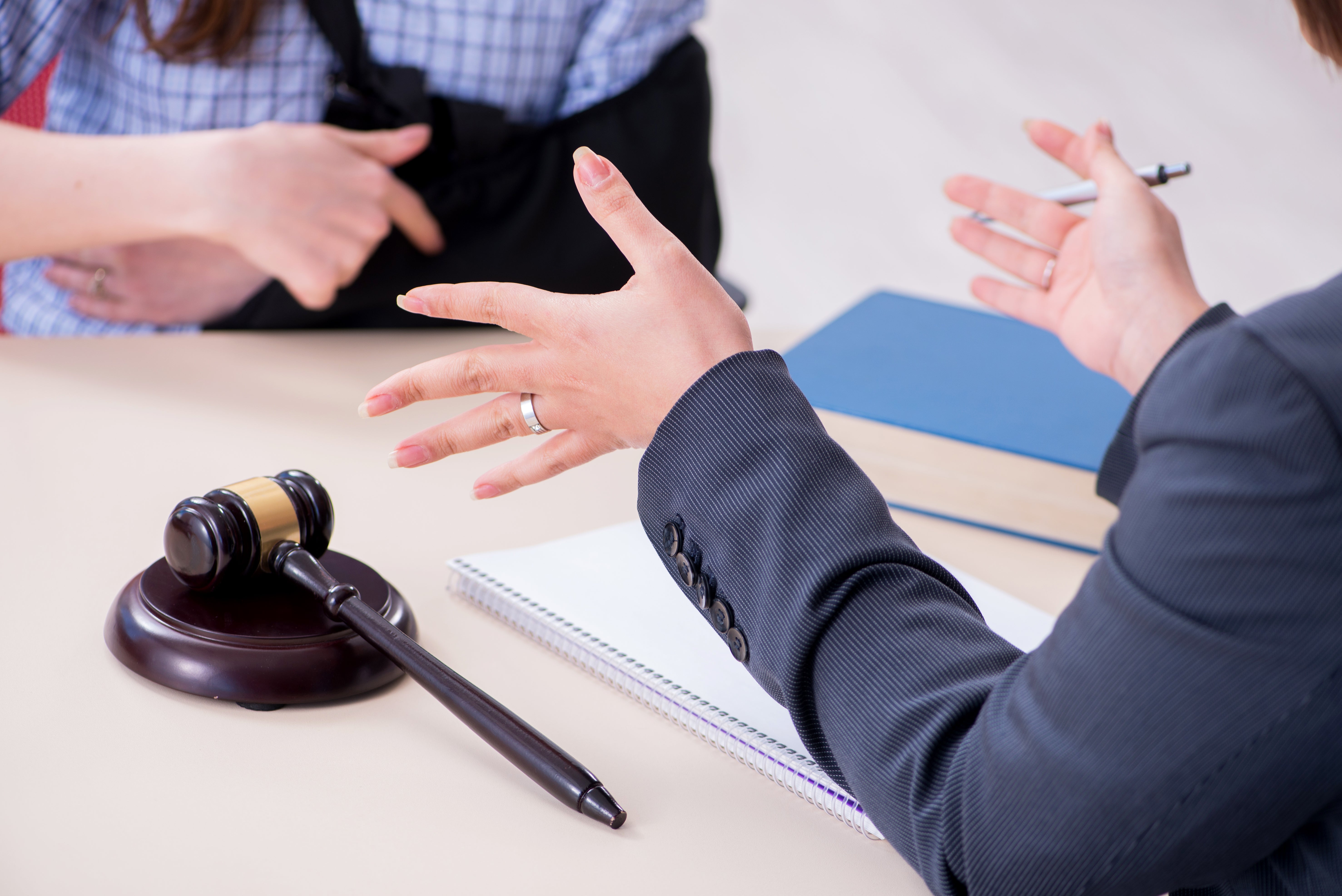Lawyer consulting with injured client wearing arm sling, discussing legal case with gavel and documents on desk.