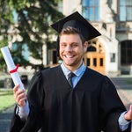 Smiling young man in black graduation cap and gown holding diploma on college campus, representing 18-year-old adults who need estate planning documents