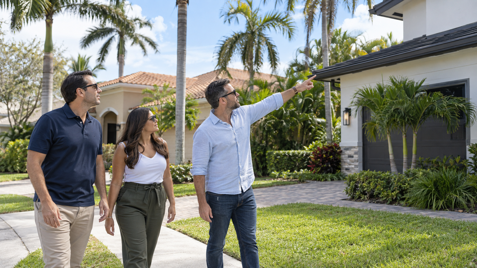 Three adult real estate investors walking outside neighboring rental homes in a South Florida neighborhood while one points toward a roofline and the others observe the property exterior.