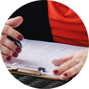 Close-up of a person's hands holding a pen and writing on a sheet of paper on a clipboard.