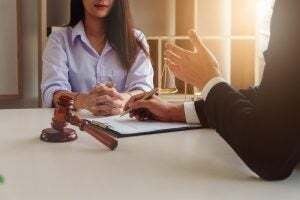 lawyer sitting across from a client with a document and a gavel on the desk.