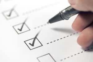Hand with black pen marking on checklist box.