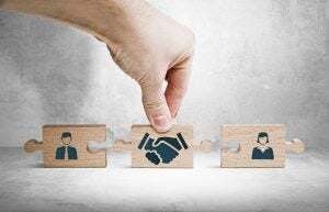 Wooden blocks with an icon of a woman and a man. In between them is a hand holding a wooden block with a handshake on it.