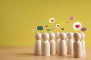 Wooden peg dolls against a yellow backdrop with emojis over their heads
