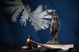 South Carolina US state flag with statue of lady justice, constitution and judge hammer on black drapery.