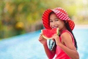Child with watermelon in swimming pool. Summer sun and water fun. Healthy fruit snack for kids. Tropical fruits in family vacation. Travel with children. Little girl on beach holiday.