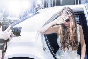 famous celebrity getting out of a limousine in front of a red carpet event, with flashing paparazzi