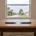 Two fountain pens on a bare table in a Punta Gorda home, representing the two witnesses Florida requires for a valid will