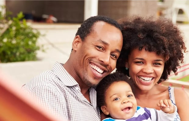 Familia negra sonriente de tres personas al aire libre: hombre, mujer y bebé.