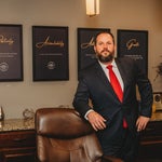 Joshua Wilson, family law attorney in Cass County, Missouri, standing confidently in his Raymore office in a navy suit and red tie