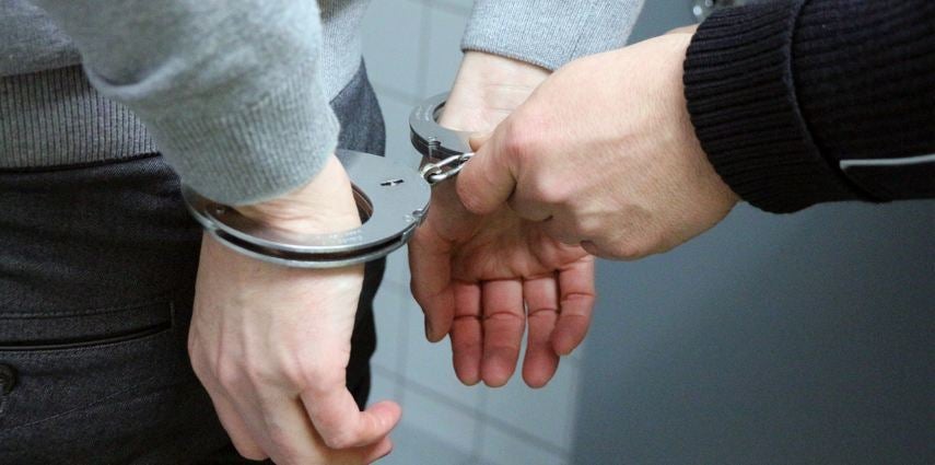 Person putting handcuffs onto another person.